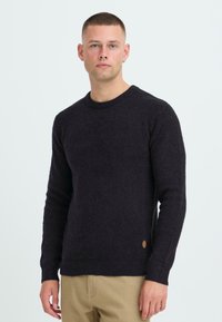 Dunkelblauer, gerippter Strickpullover mit Rundhalsausschnitt, langen Ärmeln und einem kleinen, markierten Badge an der unteren Seite. Strukturierter Stoff.
