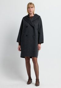 Mørkegrå uldfrakke med stor hætte, dobbeltknaplukning og to forlommer. Enkel, struktureret design med brede ærmer.