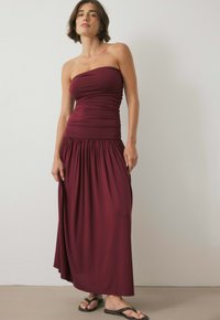 Bordó strapless maksi-kleid med gathered bodice og flydende nederdel. Glat stof, afslappet pasform, båret med sorte flip-flops.