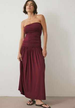 Bordó strapless maksi-kleid med gathered bodice og flydende nederdel. Glat stof, afslappet pasform, båret med sorte flip-flops.