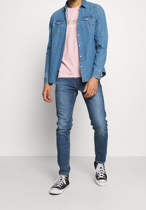 Denim shirt in light blue with pockets, pink graphic t-shirt underneath, blue jeans, and black high-top sneakers with white soles.