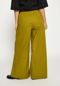 Laia säärega oliivrohelised püksid tekstuurse kangaga, millel on elastne vöökoht ja küljetaskud, kombineeritud mustade jalanõudega.