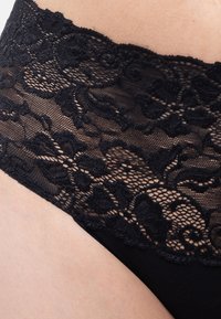 Schwarze Spitzenunterwäsche mit kunstvollen floralen Mustern am Bund und einem glatten Gewebe, das ein zartes und dennoch komfortables Design bietet.