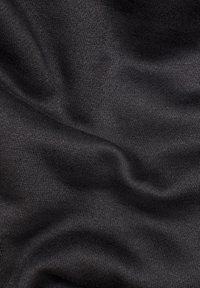 Tessuto di maglia nero con una texture morbida e un leggero grado di elasticità, caratterizzato da pieghe lisce e ondulate su uno sfondo scuro.