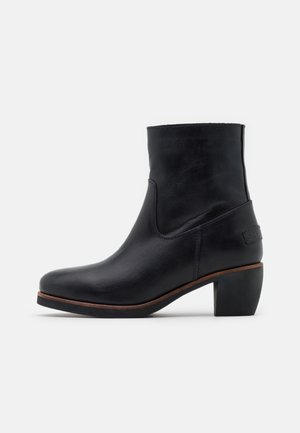 Bottine en cuir noir avec talon bloc de hauteur moyenne et bout arrondi, présentant une discrète bordure brune le long de la semelle.
