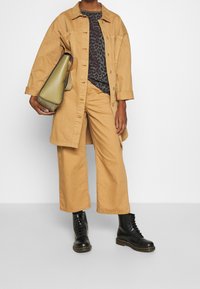 Tan cotton overshirt, leopard print T-shirt, matching wide-leg trousers, and black lace-up boots. Olive green handbag with a structured design.