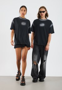 Sorte oversized t-shirts med gradient design og et lille centralt logo, parret med sorte shorts og slidte grå jeans. Sorte platform sandaler.