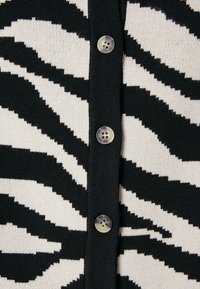 Black and white zebra-patterned knit cardigan featuring a textured surface and five button closures with a glossy finish.