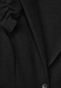 Musta neuletakki, jossa on teksturoidut kankaat, pyöreä kaulus ja yksi nappisulku, sekä kerroksellinen yksityiskohta olkapäällä.