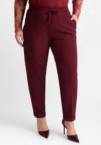 Burgunderfärgade tapered byxor med elastisk midja och dragsnodd, med uppvikta benslut och en slät tygtextur.