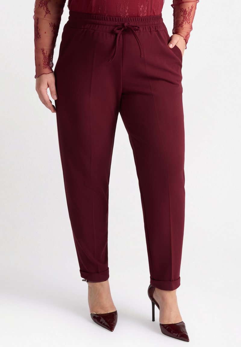 Burgunderfärgade tapered byxor med elastisk midja och dragsnodd, med uppvikta benslut och en slät tygtextur.