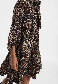 Abito con stampa leopardata caratterizzato da una scollatura con fiocco, maniche lunghe a sbuffo e un tessuto morbido e fluido con una combinazione di colori blu scuro e beige.