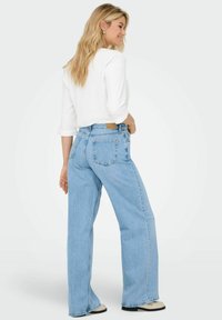 Lyseblå denimjeans med avslappet passform, høy midje, baklommer og subtile søm-detaljer. Kombinert med en hvit topp.