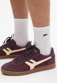 Lilla sneakers med cremefarvede accenter, lavet af mesh og syntetisk materiale. Brun gummisål, snøret front, parret med hvide ribbede sokker.