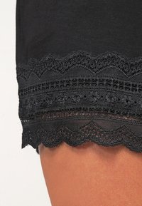 Ourlet en tissu noir avec bordure en dentelle superposée à festons et motifs floraux au-dessus de la peau nue.