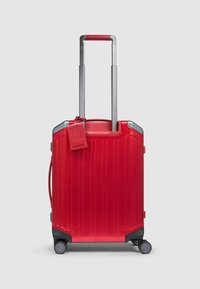 Rode harde koffer met verticale geribbelde structuur, intrekbare zilveren metalen handgreep en vier zwarte wielen. Inclusief identificatielabel.