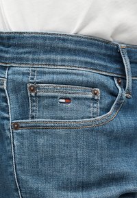 Κοντινό πλάνο τσέπης μπλε τζιν με μικρό κόκκινο, λευκό και μπλε ορθογώνιο λογότυπο και εμφανείς ραφές.