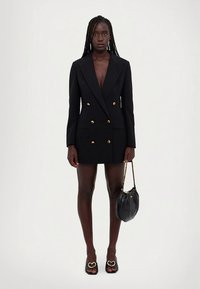 Melna divrindu žakete kleita ar zelta pogām, gluda auduma, ass atloks, pieguloša forma, kopā ar melnu rokassomu un sandales ar sirds detaļām.