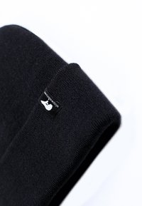 Czarna dziana czapka z teksturowaną powierzchnią i małą tkaną metką z białym logo. Design jest prosty i dobrze dopasowany.