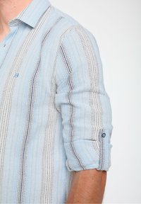 Camicia a righe blu chiaro e bianca con un tessuto testurizzato, dotata di polsini con bottoni e sottili accenti blu navy lungo le righe.