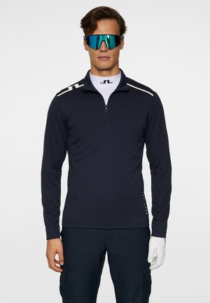 Marineblauer Pullover mit langen Ärmeln und einem Viertelreißverschluss, der weiße Akzente an den Schultern und ein tailliertes Design aufweist. Glattes, leichtes Material.