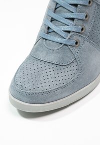 Blue suede sneaker featuring perforated detailing, flat laces, and a grey rubber sole. Close-up view highlights texture and construction.