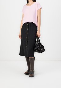 Ljusrosa t-shirt med kort ärm, svart midi-kjol med framknappar, bruna knähöga stövlar och svart handväska med blommönster.