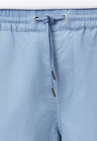 Bañadores de color azul claro con cintura elástica, que presentan un cordón anudado y ojales de metal plateado, hechos de una tela suave y ligera.