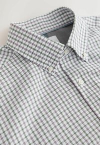 Chemise blanche à boutons avec un motif à carreaux verts et rouges, dotée d'un col boutonné et de boutons de type perle.