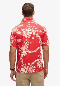 Camiseta roja de manga corta con un diseño floral blanco que incluye hojas y flores. El material parece suave y ligero, con un ajuste casual.