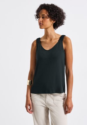 Top nero senza maniche con scollo a V, dotato di dettagli arricciati sulle spalline. Texture liscia, abbinato a pantaloni chiari.