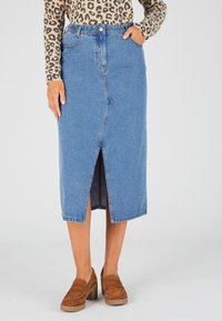 Falda midi de mezclilla en azul claro con abertura frontal, con una cintura clásica y dos bolsillos laterales, combinada con mocasines de tacón marrones.