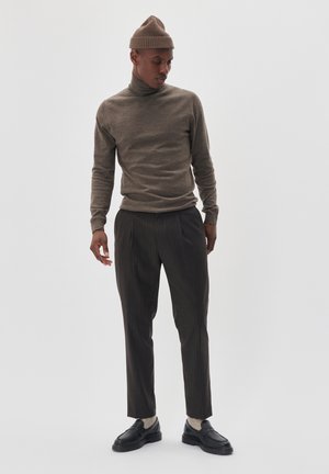 Căciulă tricotată maro, pulover cu gât închis maro, pantaloni întunecați cu dungi, și loaferi negri cu șosete gri. Materiale texturate, siluetă elegantă.