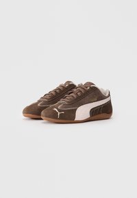 Brown suede sneakers with a white side stripe, textured laces, and a gum rubber sole. Features a small logo on the side and top.