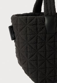 Quilted sort stof tas med en struktureret overflade, der har trekantede mønstre og et håndtag i sort læder. Inkluderer et lille brandingmærke.