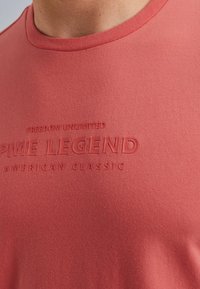Červené bavlněné tričko s kulatým výstřihem, měkkou texturou a embossovaným potiskem "FREEDOM UNLIMITED PME LEGEND AMERICAN CLASSIC."