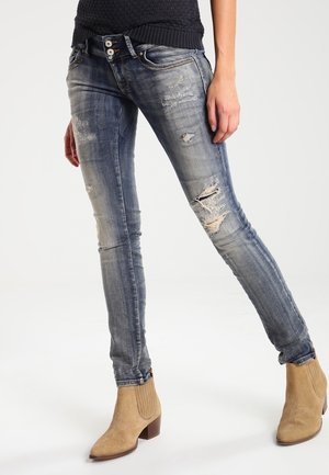 Slim-fit faded blue jeans with distressed patches worn with tan suede ankle boots and a black textured top.