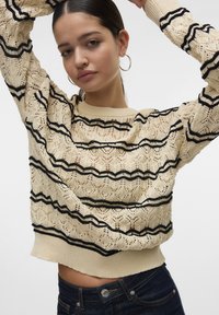 Maglione lavorato a maglia color crema con strisce zigzag nere; leggero, con una texture simile a pizzo, scollatura rotonda e polsini a costine.