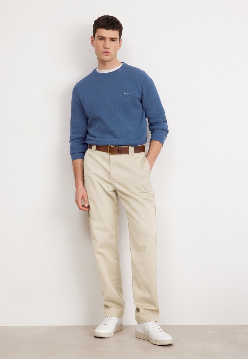 Suéter azul texturizado, pantalones beige, cinturón marrón y zapatillas blancas. Conjunto informal con un ajuste cómodo. Diseño simple y colores neutros.