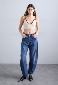 Bralette all'uncinetto color avorio con dettagli rossi, abbinato a jeans in denim azzurro chiaro e stivali neri alla caviglia con dettagli argentati a punta.