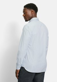 Hellblaues, langärmliges Hemd mit durchgehender Knopfleiste und vertikalen weißen Streifen. Verfügt über einen klassischen Kragen, abgerundeten Saum und taillierte Manschetten.