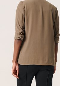 Khakiowa bluzka z podwiniętymi rękawami, gładka tkanina, luźny krój i prosty dół, w połączeniu z dopasowanymi czarnymi spodniami, widok od tyłu.