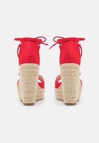 Décolleté rosse in suede con zeppa e una piattaforma rivestita di corda naturale, dotate di due lacci per le caviglie e un design aperto per la traspirabilità.