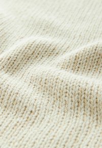 Pletená látka v mäkkej off-white farbe s textúrovaným vzorom. Obsahuje rôzne detaily stehov, čo vytvára jemný, uvoľnený rippel efekt.