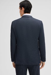 Giacca di abito blu navy su misura con tessuto strutturato, spalle rigide e tre bottoni su ciascun polsino, vista da dietro.