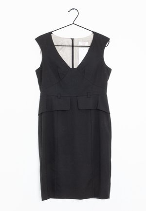 Robe noire sans manches, longueur au genou, avec décolleté en V et détail péplum, suspendue à un cintre noir sur un fond blanc.