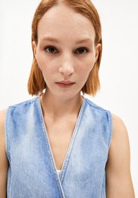 Helles Denim-Oberteil mit tiefem V-Ausschnitt und ärmellosem Design, das sichtbare Nähte und eine weiche Textur aufweist.