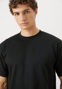 Black crew neck t-shirt made of soft fabric, featuring a relaxed fit with short sleeves and a smooth texture. No visible patterns.