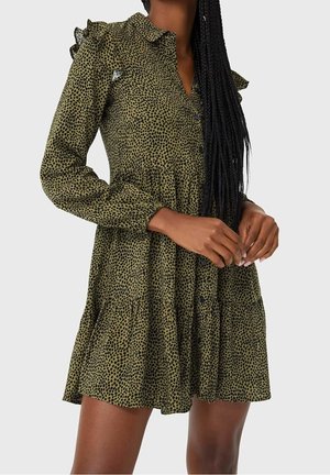 Olivgrünes Mini-Kleid mit langen Ärmeln, schwarzem Punktmuster, gestuftem Rock, durchgehender Knopfleiste und kleinen Schultervolants.