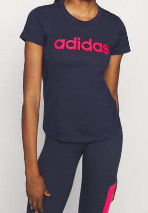 Osoba nosząca granatowy t-shirt Adidas z różowym logo i dopasowane granatowe legginsy z pionowym różowym paskiem.